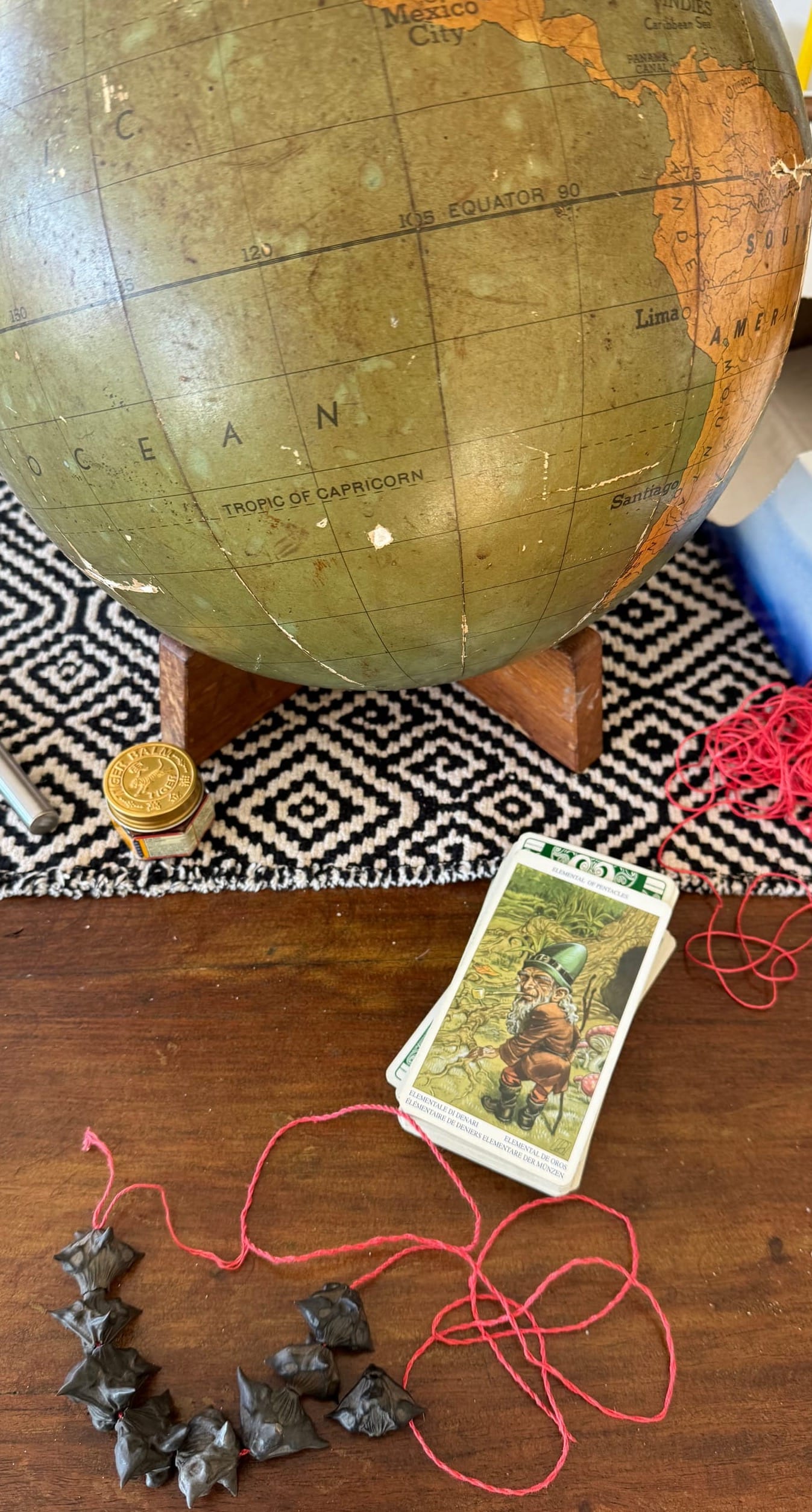 Some sea beads on a string, harvested from the banks of the Hudson River, and a tarot card with a leprechaun and some mushrooms in it, squinting at the view. There's also an old globe and a jar of tiger balm. 